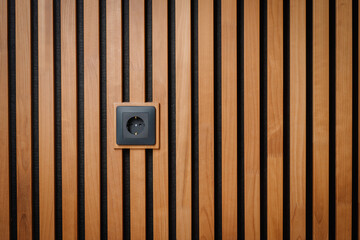 Black outlet plug on the wooden wall. Socket and European Power in the New Flat. Acoustic fluted wood panel. - obrazy, fototapety, plakaty
