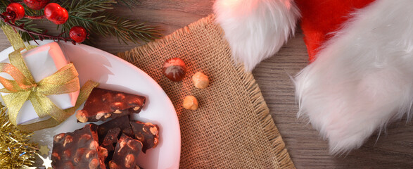 Chocolate with hazelnuts on wooden christmas table with santa hat