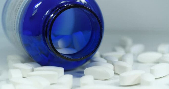 Overdose. Big white pills scattered on table. Open blue container for nutritional supplements lies on table. In reality these are biologically active sulfur pills in dosage of 1500 mg. MSM for joints