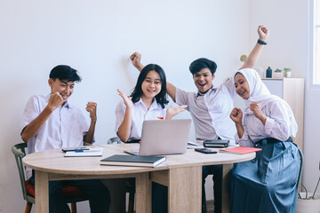 Group of multiethnic asian students in school uniform looking at laptop on desk celebrating success school project, finishing assignment, its a wrapped.
