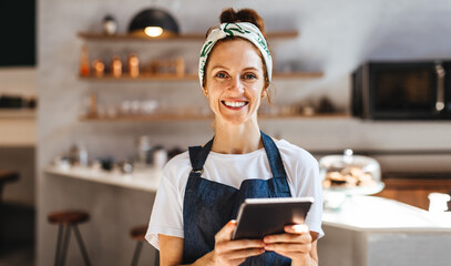 Successful cafe owner using a tablet to manage her small business - obrazy, fototapety, plakaty