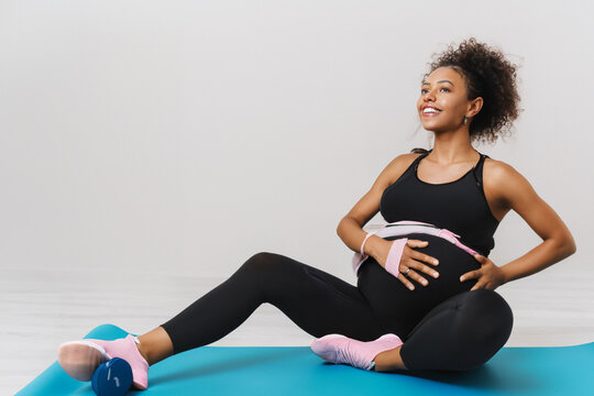 a young pregnant girl in a black elastic suit does exercises on a blue rubber mat, a young mother does exercises