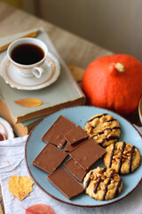 Cup of tea or coffee, plate with desserts, dried oranges, bowl of grapes, scented candles, vintage books, pumpkins and autumn leaves on the table. Autumnal hygge. Selective focus.