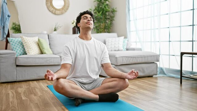 Young latin man sitting on floor training yoga stretching head at home
