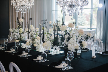 Table setting, setup. Banquet decoration composition flowers, candles in hall restaurant. Table covered black tablecloth. Luxury wedding reception. Trendy decor large chandelier for a birthday party. - obrazy, fototapety, plakaty