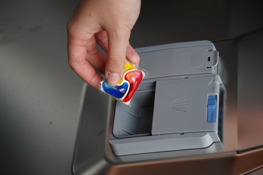 Female hand put dishwasher detergent tablet in open dish washing machine