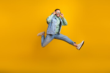 Fototapeta na wymiar Full length photo of handsome cool guy hispanic run jumping touching his sunglass positive enjoy sale isolated on yellow color background
