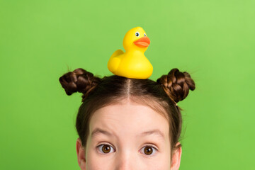 Photo of good mood impressed small schoolgirl dressed blue sweatshirt hiding with duck toy on head...