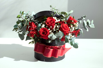 Sombrerera negra con rosas rojas y eucalipto preservado, sobre fondo neutro © ruben