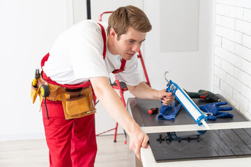 Gloved craftsman installs hob in kitchen. Household Appliance Installation Services Concept
