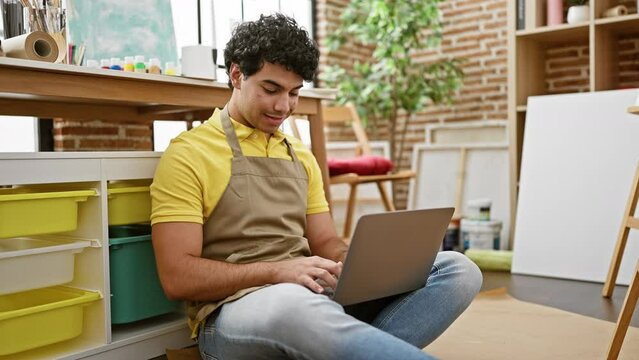 Young latin man artist smiling confident using laptop at art studio