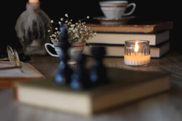 Vintage books, reading glasses, gold pen, hand model, gold jewelry, scented candles, flowers, chess pieces and cup of tea or coffee on the table. Dark academia concept. Selective focus.