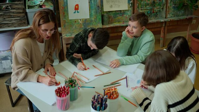 Cute female teacher paints with young students at art school