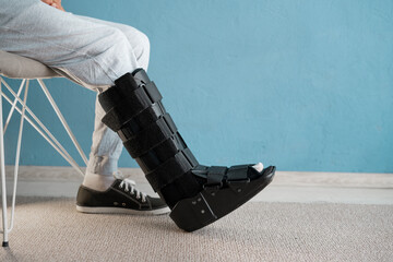 Injuried man with orthosis and sprained ankle sitting on the chair. Ankle orthosis concept