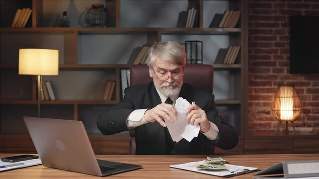 Portrait of irritated older person ripping up sheet of paper before throwing it above head at executive desk. Displeased entrepreneur in formal wear ruining written contract while sitting at work.