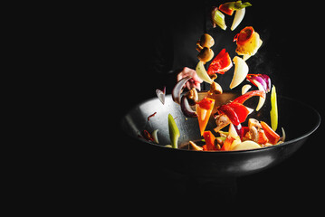 Closeup of chef throwing vegetable mix from wok pan on black background.