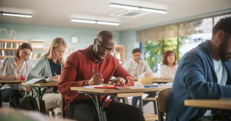 Foto op Canvas Handsome African Man Writing Down Notes in Notebook. Group of International Mature Students Studying in Classroom. Adult Training Center Help People to Develop New Useful Skills Throughout Life © Gorodenkoff