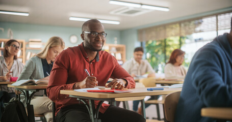 African Man Writing Down Notes in Notebook And Smiling. Group of International Mature Students Studying in Classroom. Adult Training Center Help People to Develop New Useful Skills Throughout Life © Gorodenkoff
