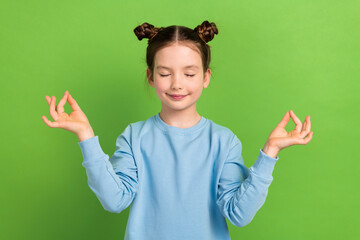 Photo of peaceful schoolgirl with buns hairdo dressed blue pullover fingers tougether eyes closed...