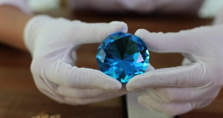 Hands of jeweler-gemologist in gloves holding large round blue diamond. Examination of stones - Powered by Adobe