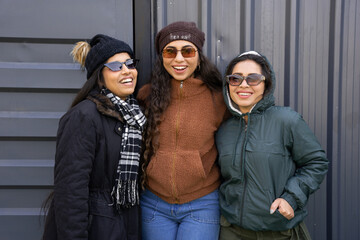 Cheerful Group of three young indian girls enjoying vacation wearing warm winter clothes enjoying. Isolated over grey background