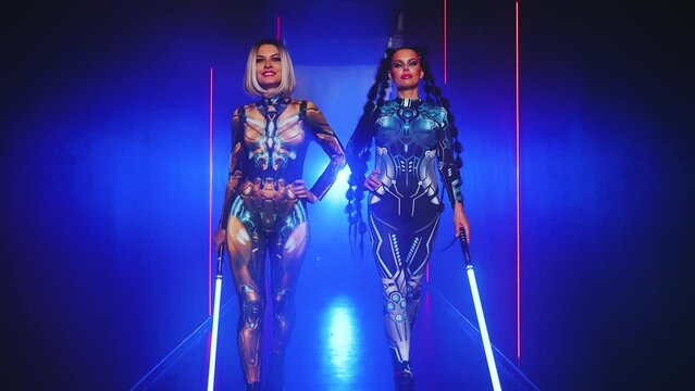 Two women cyborg creative robot costume metal body creative makeup, cyberpunk style blonde hair, braid hairstyle. Sexy alien girl in virtual reality war, woman warrior future vr laser sword in hands