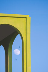 Green Tuscany arch wall style with blurred background of 2 swallows flying and moon on blue evening sky in vertical frame. Street minimal architecture background concept
