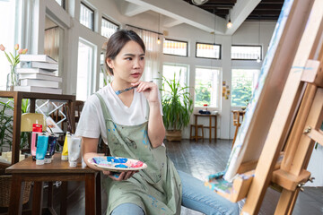 close up picture of happy young Asian woman painting brush on canvas in painting studio. In the art workshop class.