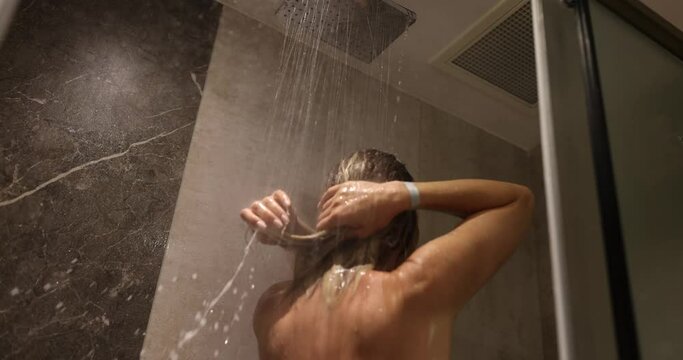 Woman washes hair with shampoo with dripping water. Take shower and relax under warm running water