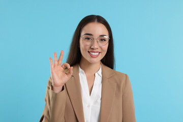 Beautiful woman in glasses showing OK gesture on turquoise background