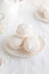 White airy zephyr or marshmallow shells on a plate on a white table, with space for text