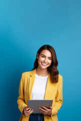 Fototapeta premium Portrait of a beautiful girl with a laptop on a blue background in a yellow jacket with a smile and dark hair