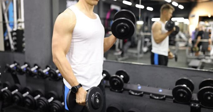 Man raises his arms with dumbbells in gym. Physical and muscle training for bodybuilding