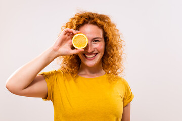 Happy ginger woman is covering her eye with slice of lemon.