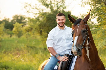 Fototapeta premium a young guy in a white shirt sits on a horse, a guy walks with his horse through the forest