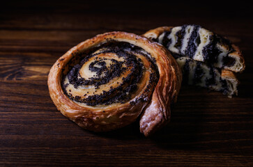 Two poppy seed buns whole and cut on a wooden background.