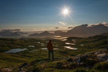 Man on a hike looking towards the late evening sun in Lofoten, Norway, during the summer.