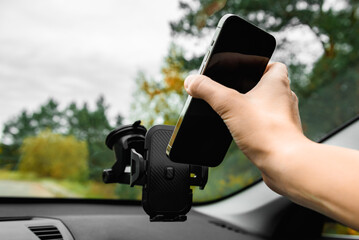 Hand putting mobile phone on car phone holder on windshield.