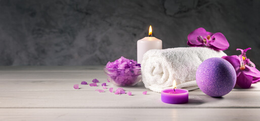 purple bath bomb, sea salt crystals, towel and scented candles on wooden table. wellness spa center. banner with copy space