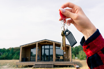 Close-up of a woman's hand holding the keys to her recently purchased wooden country house in woods