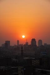 Naklejka na ściany i meble Orange and yellow open skies. Sunset over the city of Cairo in Egypt. Silhouette of the buildings in the metropolis. Neighborhood view of the cityscape.