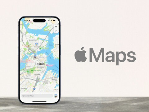 modern smartphone displaying map view of Apple Maps, standing on a stone desk in front of a gray wall with the Apple logo, navigation, route, cartography