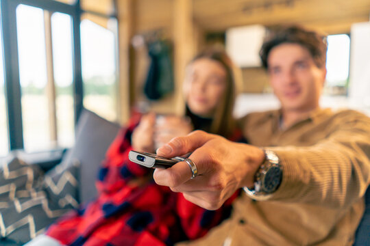 A couple in love are relaxing The man's hand is pointing the remote control at TV to change channel