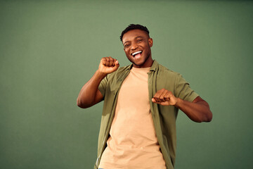 Expressing happiness. Carefree millennial guy wearing unbuttoned khaki shirt joyfully dancing with...