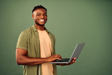 Freelancing with gadgets. Friendly african american guy standing over green studio background,...