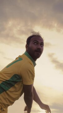 Vertical Screen: Portrait of a South Asian Cricket Player in Yellow and Green Uniform Throwing the Ball on a Pitch. Professional Indian Bowler is Focused, Aiming to Hit the Wicket With His Shot