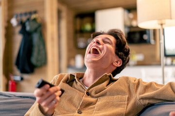 Portrait of a young guy with a TV remote in his hand watching comedy and laughing out loud