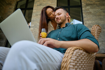 Man sits in a wicker chair and works on laptop