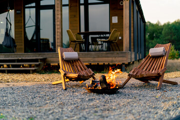 A fire is burning outdoors near a cosy wooden house with terrace in a glamping site in steppe 