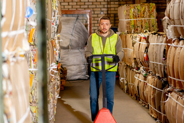 Worker in a safety vest and gloves walks down a hallway with a hydraulic pallet truck for...